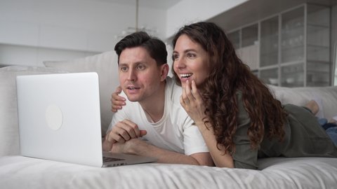 Exalted brunette wife and excited short-haired husband do online shopping for new apartment looking for discounts on sofa in living room