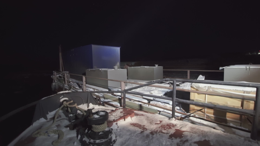 View from the bow to the pier with cargo. CLIP. Night view from the bow of a ship anchored in a winter port on the cargo that is on the pier