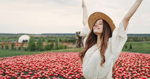 Beautiful Ukrainian Girl on the Field with Tulips Enjoys Nature Breathes Freely. Standing at the Meadow with Colorful Flowers. Wears Straw Hat, having Romantic Mood, Long Hair. Cheerful Woman. Pretty.