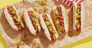 Video of hot dogs with mustard, ketchup and jalapeno on a yellow surface. food, cuisine and catering ingredients.
