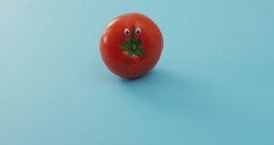 Video of fresh tomato with eyes over blue background. fusion food, fresh vegetables and healthy eating concept.