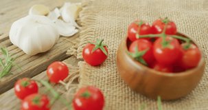 Video of fresh cherry tomatoes in bowl and garlic on rustic cloth over wooden background. fusion food, fresh vegetables and healthy eating concept.