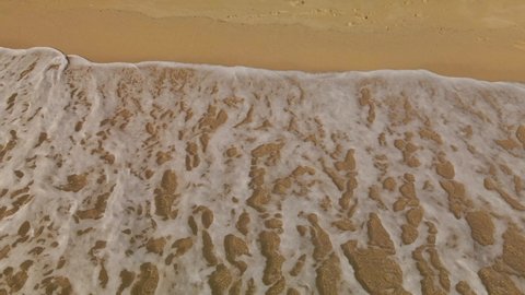 Ocean waves white sea foam rolling into a golden sand empty beach in Costa Brava, Spain
