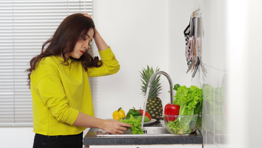 stressed young woman washing vegetables in the sink in the kitchen at home

