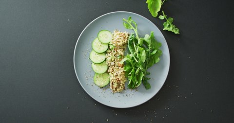 Video of fresh sliced cucumber, leaves and grains salad on grey plate over dark grey background. fusion food, fresh vegetables and healthy eating concept.