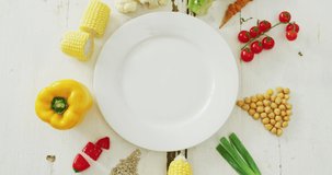 Video of fresh vegetables arranged around white plate with copy space on white rustic background. fusion food, fresh vegetables and healthy eating concept.