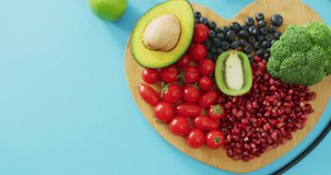 Video of stethoscope and fresh fruit and vegetables on heart shaped wooden board on blue background. fusion food, fresh vegetables and healthy eating concept.