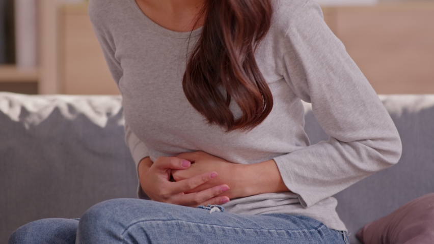 A long hair woman sitting on the couch and always squeeze on her belly.She has got stomach ache she may has a Dyspepsia or ulcer in her tummy.She not fine at all and  she has a grimace face.Woman Care | Shutterstock HD Video #1088072843