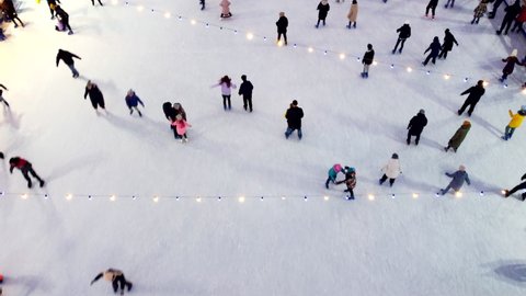 Kiev, Ukraine, January 2, 2022:-Top view of people skating on large open-air ice rink on winter day. Aerial Drone View Flight Over crowd of people who skate on ice at rink. Winter sport activities.