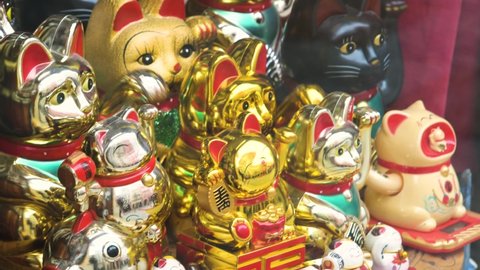 Multiple traditional Japanese maneki neko beckoning cat moving paw figurines on a store display, group of objects, tourist souvenirs sold at the store, products on display, good luck charm concept