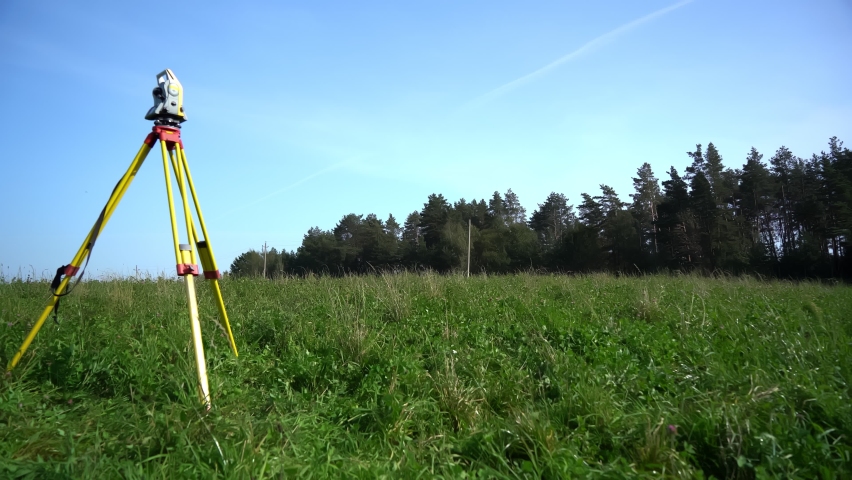 A surveyor with a reflector in his hand is moving away from the total station standing on a tripod in the field and walking towards the point to be measured. A professional surveying engineer surveys. Royalty-Free Stock Footage #1088076875