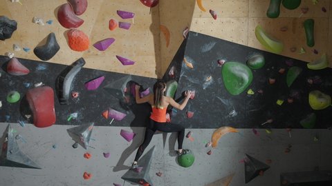 Wellness, female climber training on a climbing wall, young woman practicing rock-climbing, mountaineer training, moving up.