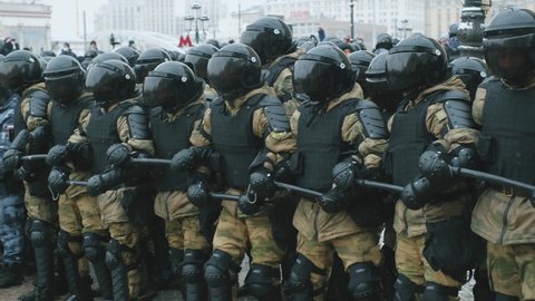 Geared and armored uniform, tinted visors on helmets, riot police team. Policeman officers with batons blocking streets for protesters by chaining arms. Enforcement group of police on demonstration.