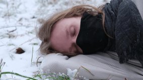 young man wearing long hair and black mask sleeping on the snow outdoor opening his eyes and wake up, slow motion video
