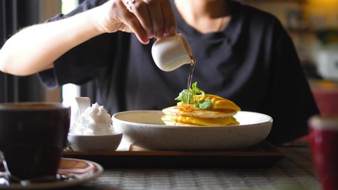 Female pours maple syrup on delicious pancakes. Young woman eating breakfast in vegan restaurant. High quality healthy food 4K slowmotion footage.