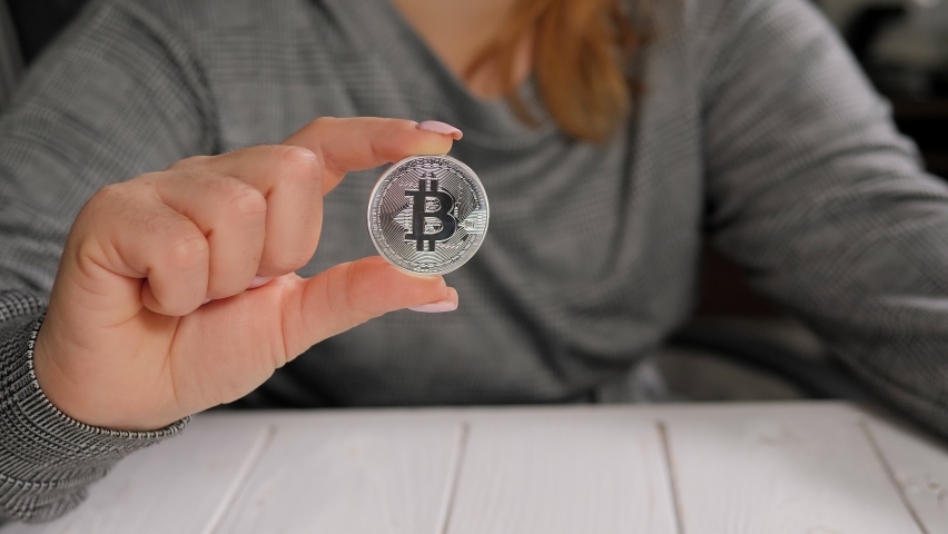 Close-up of a young woman holding a cryptocurrency coin in her hands and showing thumb down. Finance and investment concept.