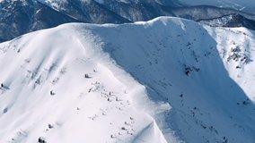 Aerial footage of snowy ridges and sharp mountains on the horizon on a sunny day