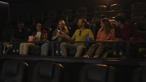 Group of young friends in a movie theater, came watching a movie on a big screen, talking to each other