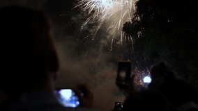 Crowd see fireworks and celebrating with photos by mobile telephone. Hand holding mobile smart phone, luxury bokeh light with firecracker background, crowd watching colorful fireworks - Powered by Shutterstock - Get 15% off with code: PIKWIZARD15