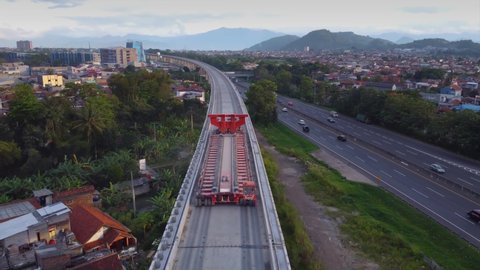 Established Aerial View of Empty Box Girder Transporter Vehicles Crossing Elevated High Speed Rails On Padaleunyi Toll Roadside