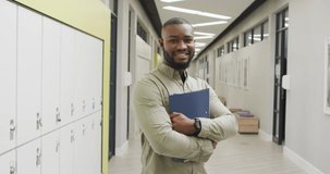 Video of happy african american male teacher standing in school hall. primary school education and teaching profession.