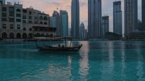 Dubai, United Arab Emirates - January 5,2022: wooden boat in lake of Dubai fountain show area near Dubai Mall and Burj Khalifa in the evening