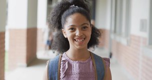 Video of happy biracial girl standing at school corridor. primary school education and learning concept.