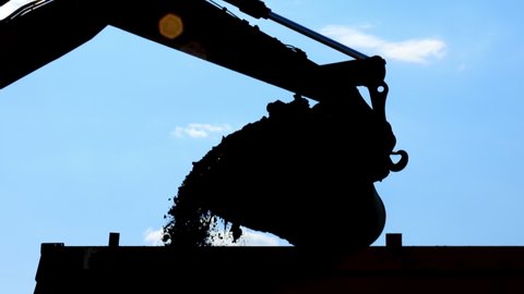 Silhouette of excavator bucket. Repair work. Construction footage. The escovator bucket pours out debris. Construction abstract background. Renovation work concept.