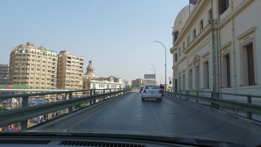 Car drives along bridge road of Cairo in sunny day. View from inside automobile. Urban architecture of modern arab city. Egyptian cityscape with houses, buildings, mosque, trees, street lamps Royalty-Free Stock Footage #1088096855