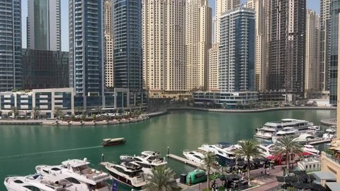 Dubai, United Arab Emirates - March 8th, 2022: View of Dubai Marina showing the luxury yachts besides the walk while small boats are crossing on a sunny day