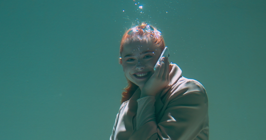 Cinematic under water portrait, happy young beautiful redhead business woman talks on mobile phone smiling slow motion.
