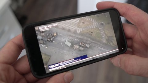 Watching the news online on a smart phone showing the Russian invasion of Ukraine. War images of destroyed buildings MONTREAL CANADA MARCH 2022