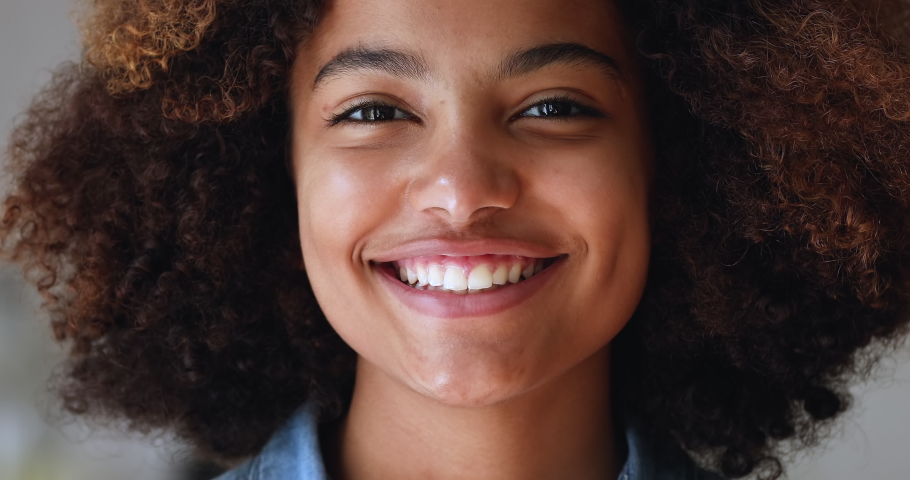 Close up cropped front face view beautiful African teenage girl with natural afro curly hairs having wide toothy smile looks at camera. Advertises dental clinic services, gen Z person portrait concept