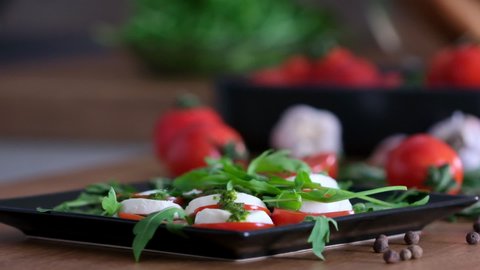 Delicious caprese salad with tomatoes, mozzarella, basil, cheese, pesto sauce, fresh arugula leaves. Pouring pesto sauce on Caprese lettuce slow motion. Healthy eating. Italian cuisine. Vegetarian 