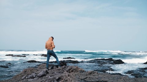 Photographer tourist man in yellow sweatshirt shooting big ocean waves on Canary Island, Tenerife
