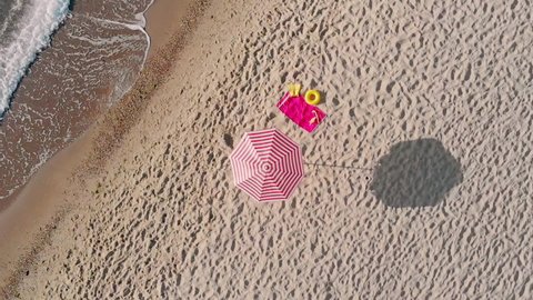 A striped beach umbrella, a red towel with flippers and a swimming mask lie on the beach, video shot from the air.