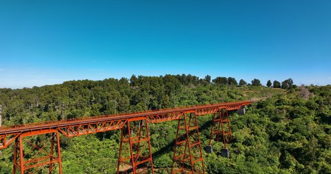 Close-up flight to bright red orange Makatote rail viaduct with forest - NZ