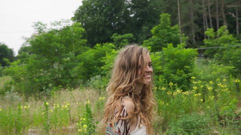 Slow motion close-up of a happy tousled blonde hippie caucasian girl walking on a rural campsite in nature