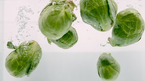 Whole Brussels Sprouts Falling into Water in Slow Motion on White Background Isolated. Fresh Vegetables Splashing into Clear Water. Healthy Food Concept. Macro