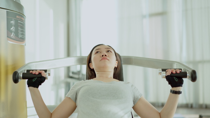 4K footage of active happy Asian young woman training a weight workout by using a shoulder press machine. Sportswoman doing a weight training exercise in the indoor gym.