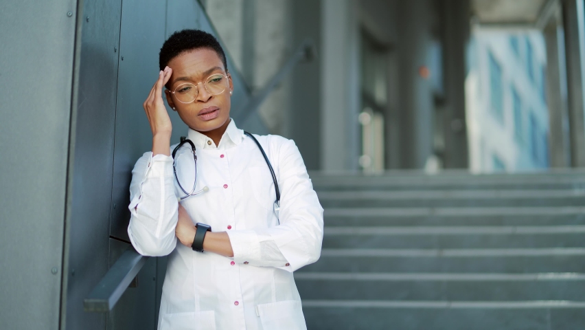 Exhausted stressful African American female doctor standing outside a hospital Tired pensive physician near clinic. Sad black woman Stress of health care worker during pandemic medic scrubs Royalty-Free Stock Footage #1088113051