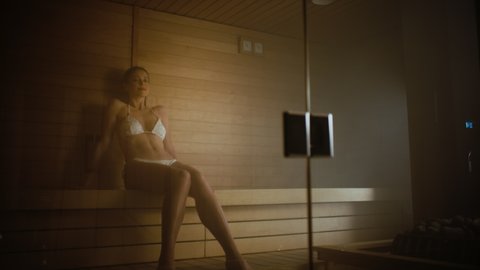 Beautiful Caucasian Female Model Sitting in the Sauna and Enjoying Her Holiday in a Slow Motion Frame. Gorgeous Brunette Looking Directly at the Camera in a Hot Sauna.