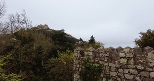 Still video looking over the ancient old castle. On top of the hill with rusty trees. Old and historic ruins. Moody weather with no sun. No people around. Moorish castle in the park of Sintra, Porugal