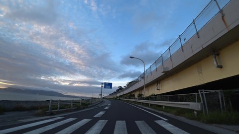 OKINAWA, JAPAN - AUG 2021 : Driving around Nago city area in sunset time. Point of view (POV), seaside road driving shot. Romantic summer holiday, vacation and travel concept.