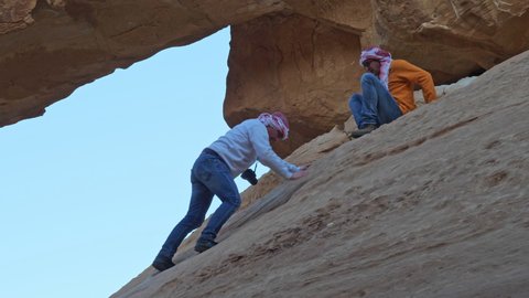 Wadi Rum Desert Jordan FEBRUARY, 03, 2018 Tourists perilously climb a steep rock face to reach a scenic natural rock bridge