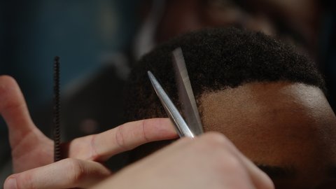 Close-up of barber cutting african american guy's haircut with scissors in barbershop