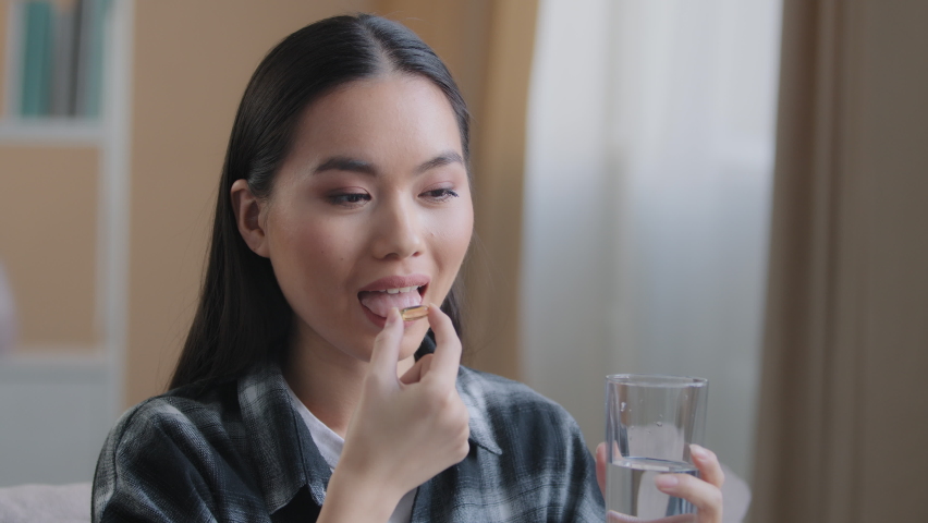 Asian race woman take drug remedy drinking glass of still water indoors at home. Korean pregnant sick girl holding pill from headache flu symptom health care medicine for disease. Dieting concept Royalty-Free Stock Footage #1088120919