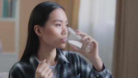 Asian race woman take drug remedy drinking glass of still water indoors at home. Korean pregnant sick girl holding pill from headache flu symptom health care medicine for disease. Dieting concept