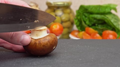 Slicing brown champignon mushrooms, chopping champignon with a knife on a cutting board, preparing healthy food