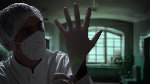 Scary caucasian doctor puts on medical gloves in an abandoned asylum. Close-up in dark old hospital. High quality 4k footage